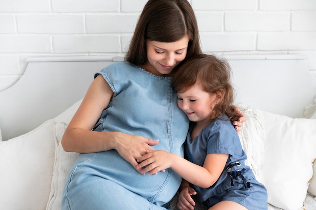 Long shot pregnant mother and daughter staying in bedroom