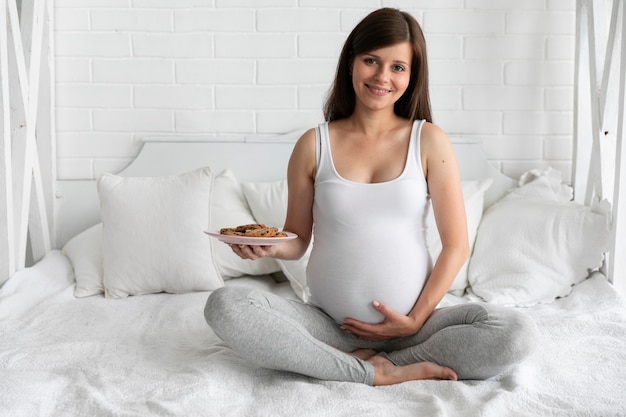 Free photo long shot pregnant woman holding a plate of cookies