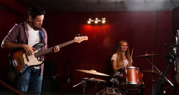 Long shot view of woman playing drums and man playing guitar