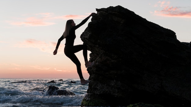 Long shot woman climbing a rock next to the ocean