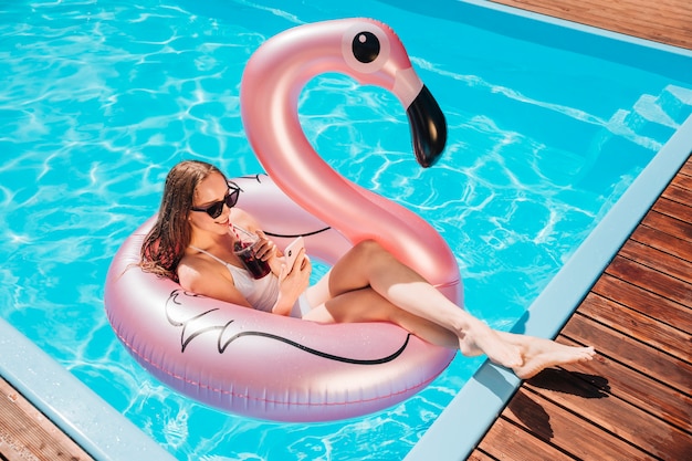 Long shot woman having a drink in swim ring