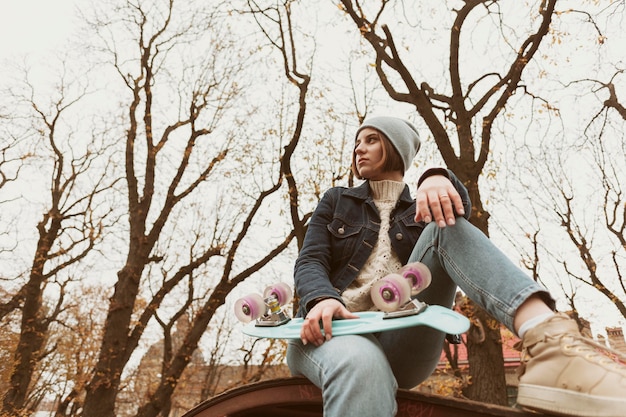 Foto gratuita donna del colpo lungo che tiene uno skateboard