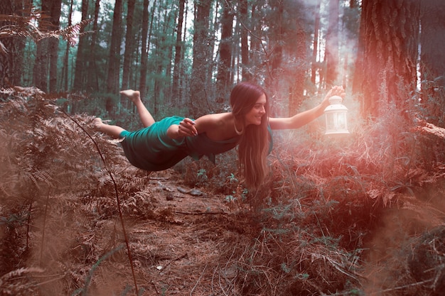 Free photo long shot woman levitating in the forest with lantern