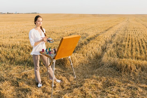 Long shot woman painting in the nature