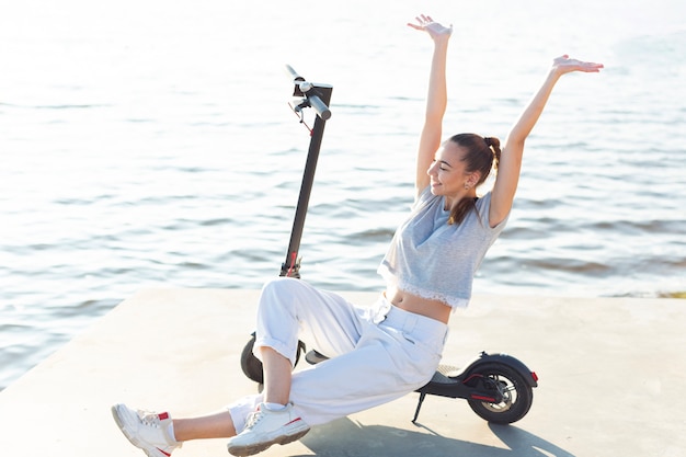 Long shot woman posing on scooter with her hands up