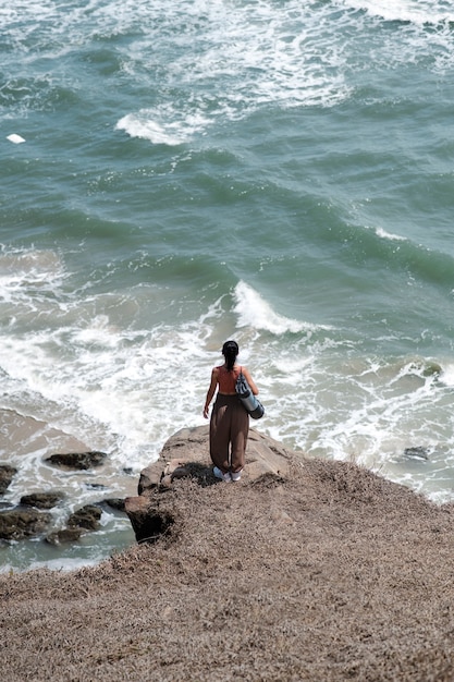 Женщина с длинным выстрелом на берегу моря с ковриком для йоги