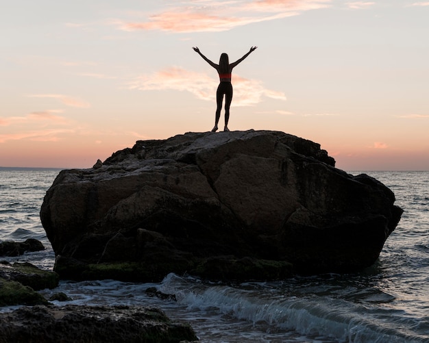 Бесплатное фото Длинный выстрел женщина, стоящая на большой скале в океане