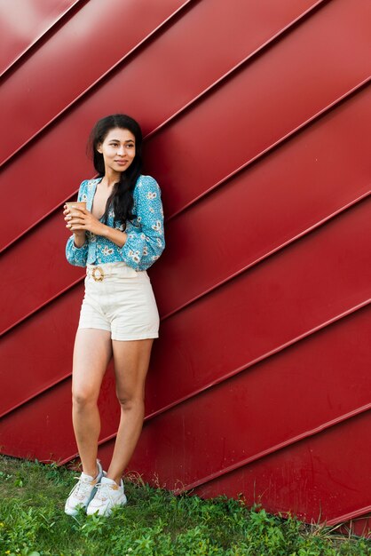 Long shot of woman with floral shirt leaning on a red tin background