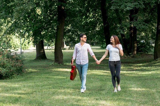 Long shot young couple walking through meadow hand in hand