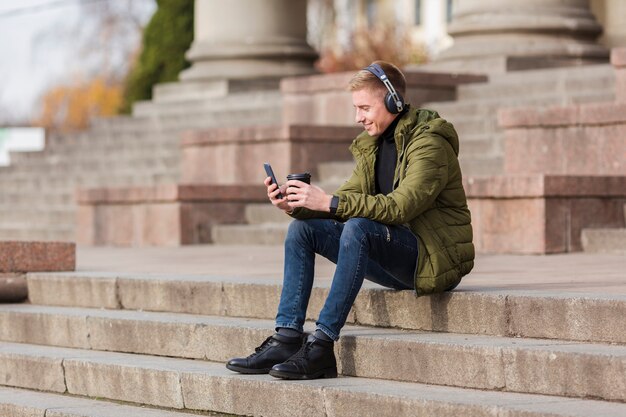 Long shot young man listening to music on headphones outside