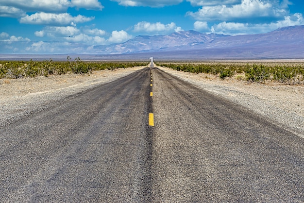 Long straight concrete road in between the desert field