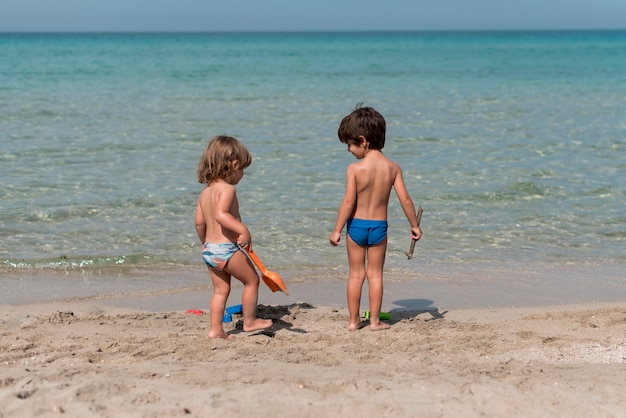 Длинный вид детей, стоящих на пляже с игрушками
