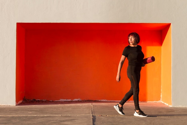 Long view of woman holding a fitness mat