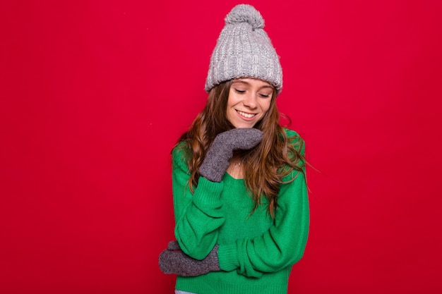 longhaired young woman in green sweater and grey knitted cap laughing on red