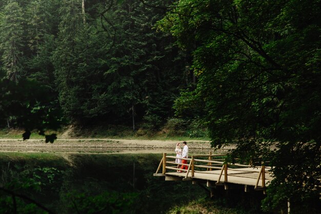 Look from afar at lovely couple standing on wooden porch over mountain lake