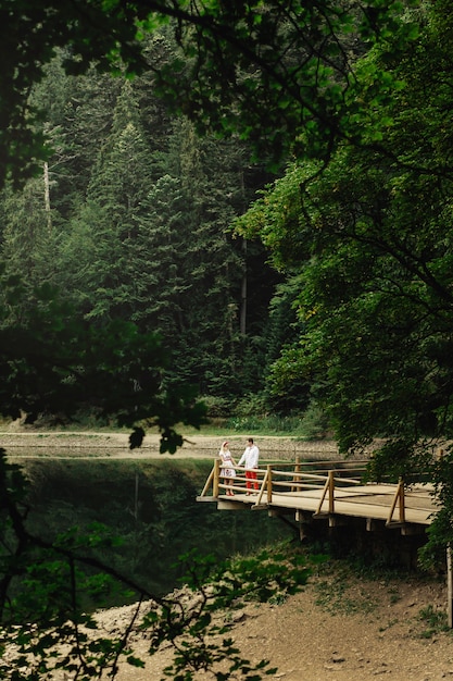 Look from afar at lovely couple standing on wooden porch over mountain lake