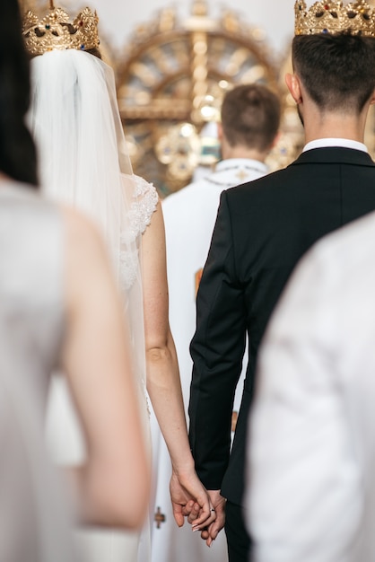 Бесплатное фото Посмотрите сзади на свадебную пару, стоящую в коронах во время церемонии
