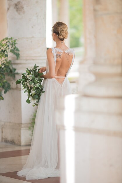 Look from behind at bride with tattoos standing between the columns