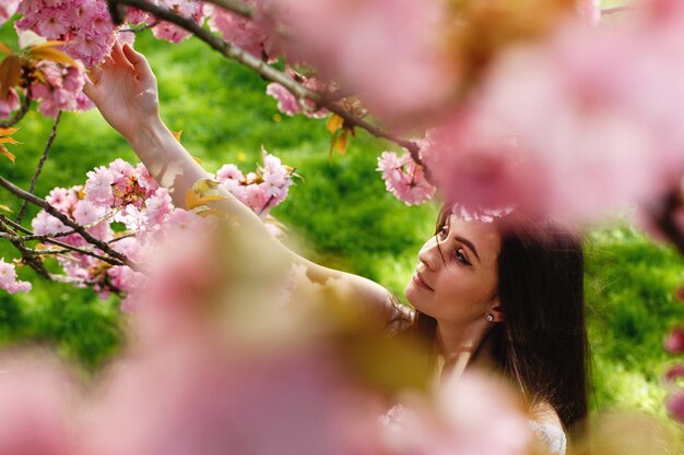 Look from above at charming young woman standing under blooming sakura tree