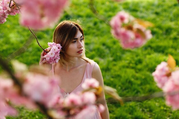 Look from above at charming young woman standing under blooming sakura tree