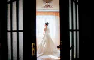 Free photo look from behind the door at a pretty bride standing in a luxury hotel room