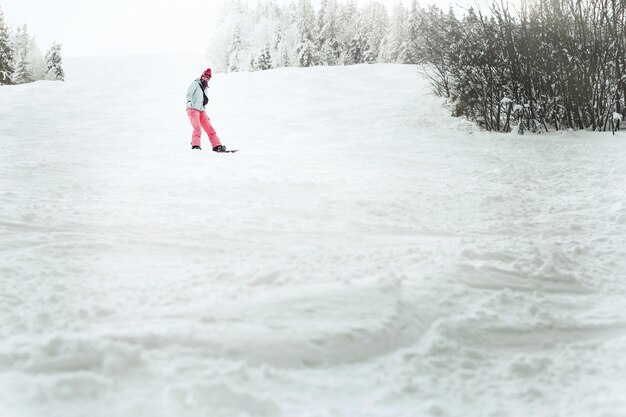 彼女のスノーボードの丘を下っている青いスキージャケットの女性の下から見てください