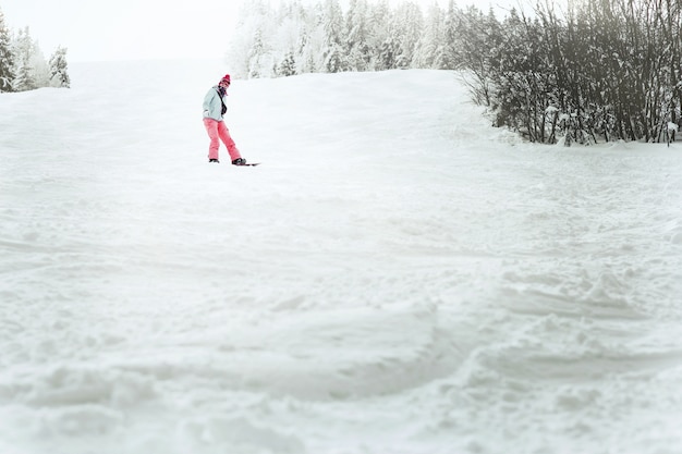 Посмотрите снизу на леди в голубой лыжной куртке, спускающейся с холма на ее сноуборде