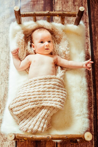 Look from above at little baby lying on wooden bed with white fu