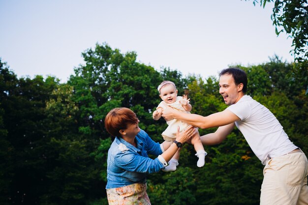 Look from below at man and woman playing with daughter in the forest 