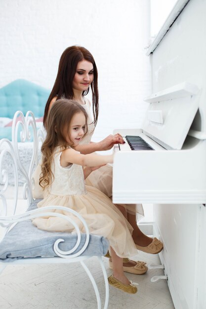 Look from behind at mother and daughter playing white piano