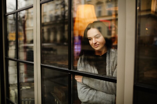 Look from the outside at a charming woman standing thoughtful behind the window