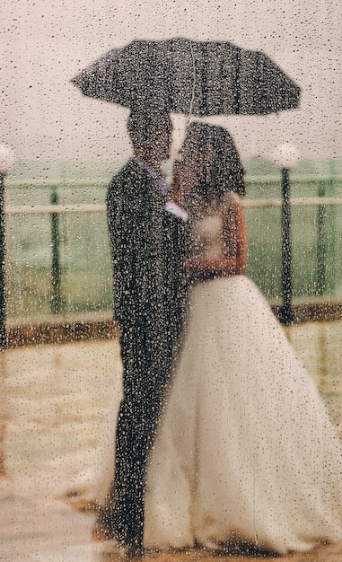 Free photo look from behind the window at wedding couple standing under umb