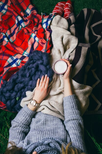 Look from above at woman lying under colorful plaids with cup of latte