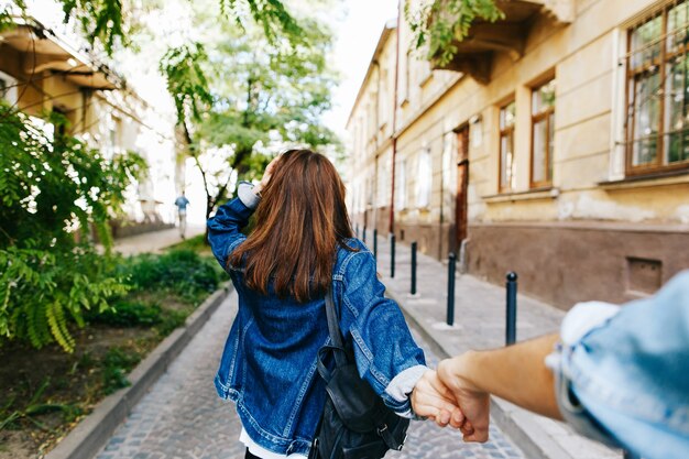 Look from behind at young woman holding man's hand in 'Follow me' pose