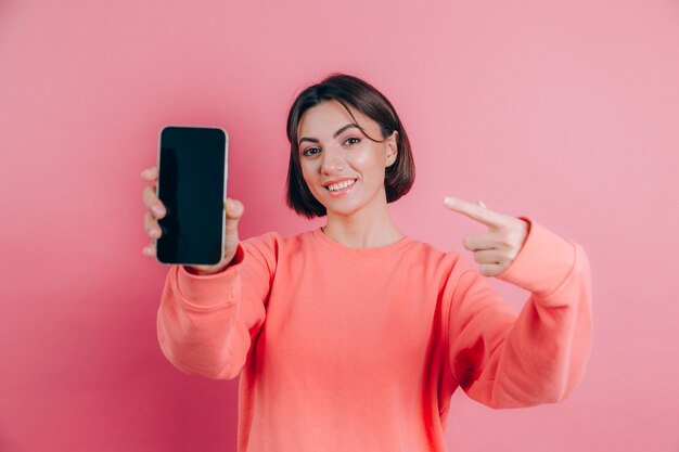 Look at this cell phone! Pleased happy woman points with index finger at blank screen, shows modern device, happy surprised emotions.