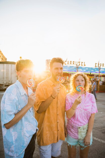 Looking away friends licking lollypop at funfair