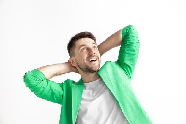 Looking for the best moment. Young dreaming smiling man is waiting for chanses isolated on gray background. Dreamer at studio in white T-shirt