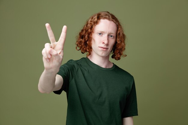 Looking at camera showing number young handsome guy wearing green t shirt isolated on green background