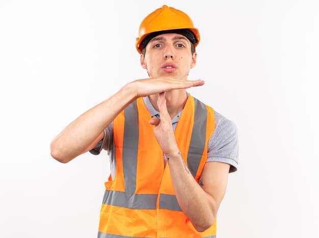 Looking at camera young builder man in uniform showing timeout gesture 