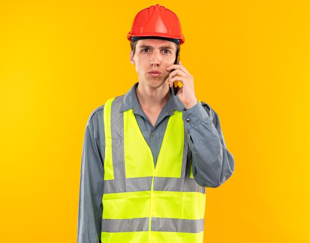 Looking at camera young builder man in uniform speaks on phone 