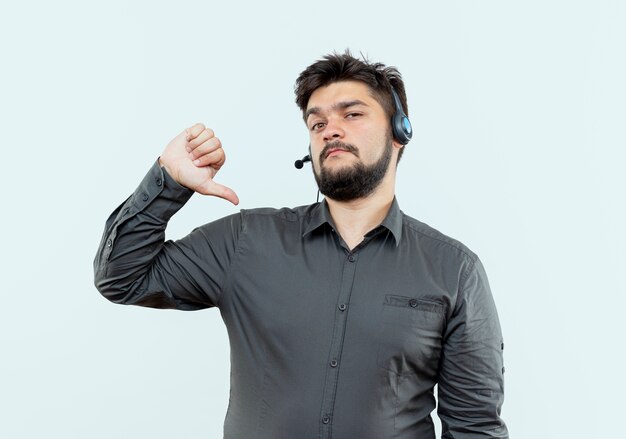 Looking at camera young call center man wearing headset his thumb down isolated on white background