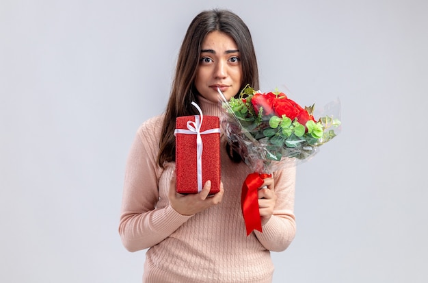 Молодая девушка смотрит в камеру на день святого валентина, держа подарочную коробку с букетом на белом фоне