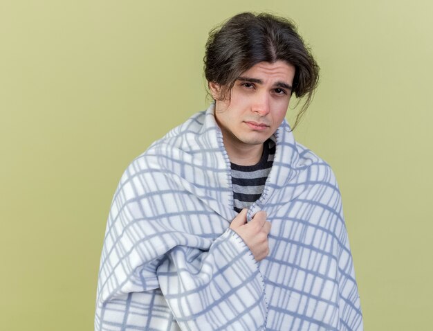 Looking at camera young ill man wrapped in plaid isolated on olive green