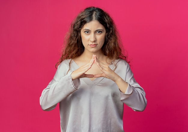 Looking at camera young pretty girl holding hands together isolated on pink background