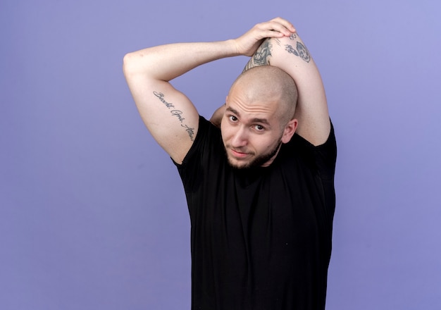 looking at camera young sporty man stretching hand behind head isolated on purple