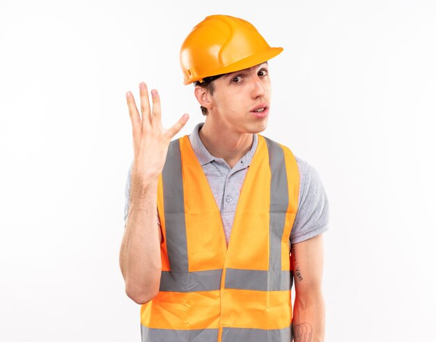 Looking at front young builder man in uniform showing four isolated on white wall