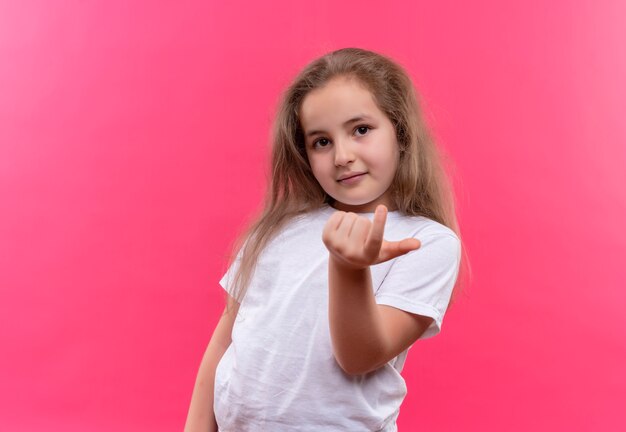 孤立したピンクの背景にここに来るジェスチャーを示す白いTシャツを着ている小さな女子高生を探しています