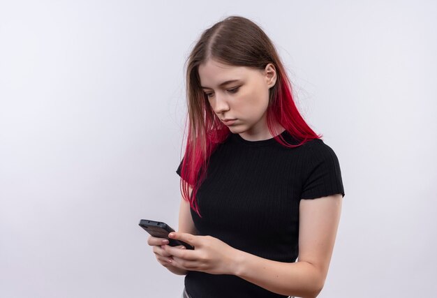 Looking at phone young beautiful woman wearing black t-shirt dial number on isolated white wall