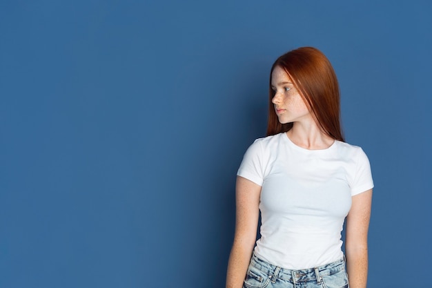 Looking at side. Caucasian young girl's portrait on blue wall