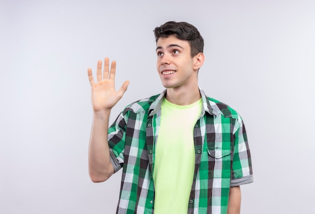 Looking at side caucasian young man wearing green shirt givening greet on isolated white wall